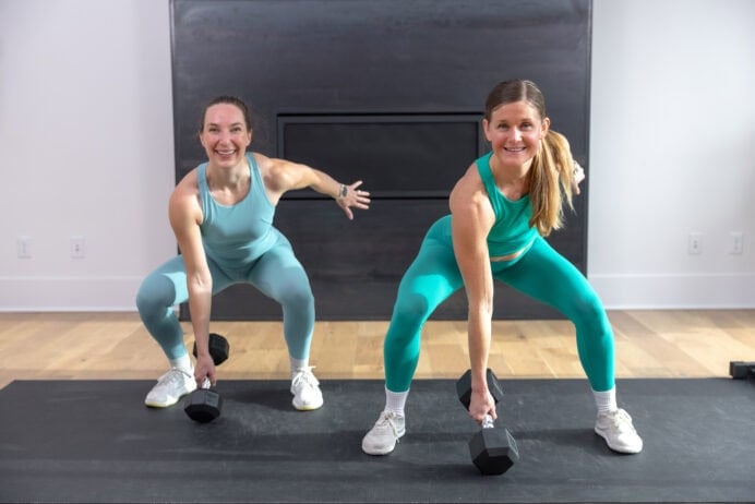 two women performing a dumbbell squat jack as part of the best EMOM exercises